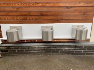 Three silver wall mounted water drinking fountains placed on the wooden wall. 