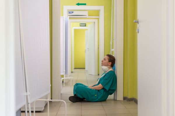 Carehome worker, wearing scrubs, sitting on the floor in a hallway