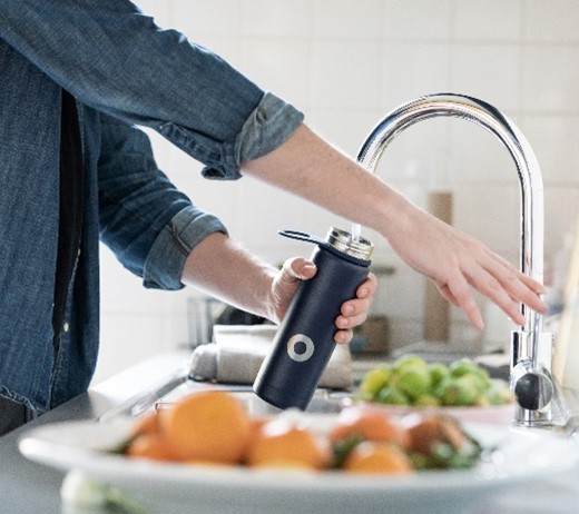 Person filling up their water bottle in a modern kitchen sink.