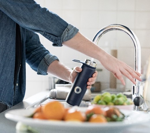 Person filling up their water bottle in a modern kitchen sink.