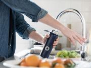 Person filling up their water bottle in a modern kitchen sink.